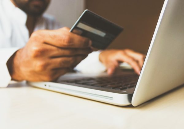 Hand holding a credit card while typing on a laptop, representing the Franchise Ops Companion App project